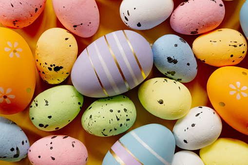 Close-up of a woman hands holding stacked bowls full of pastel colored Easter eggs. Hand holding up a bowl filled with eggs in various colors.