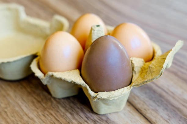 Eggs in a cardboard box on a wooden table, close-up. Chocolate egg along with raw eggs. Happy easter.