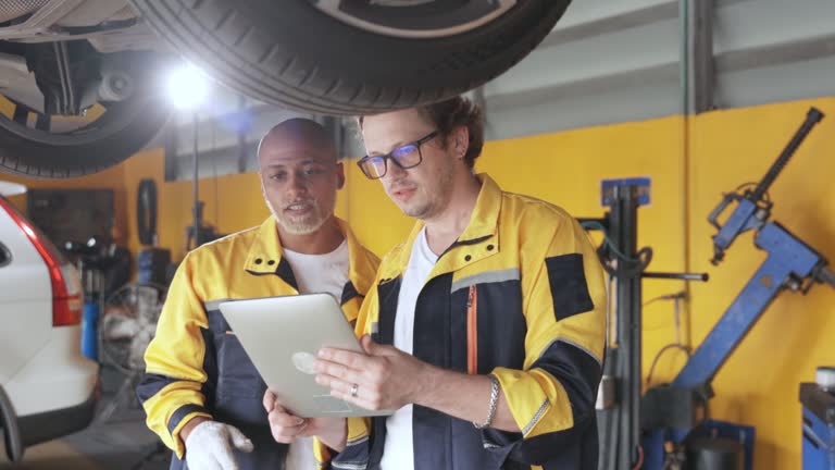 Two mechanics in a car repair shop are discussing repairs to the underbody and suspension of an old car