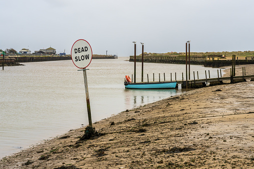 Walberswick, Suffolk, England, UK - November 17, 2022: Sign Dead slow and a boat at the shore of the River Blyth