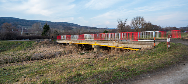 Old bridge over stream with red and white railings.