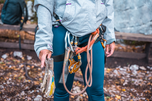 Close-up view of a person's midsection, showing hands equipped with safety harness and gloves, ready for a zipline adventure. The individual's casual outdoor attire suggests an active, adventurous setting.