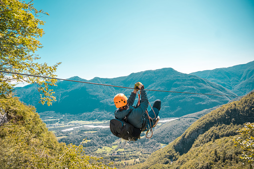 Young black male soaring through mountain peaks on an exhilarating zip-line adventure embracing nature's grandeur with breathtaking views and adrenaline-pumping thrills.
