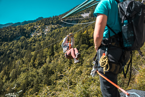 Young female soaring through mountain peaks on an exhilarating zip-line adventure embracing nature's grandeur with breathtaking views and adrenaline-pumping thrills.