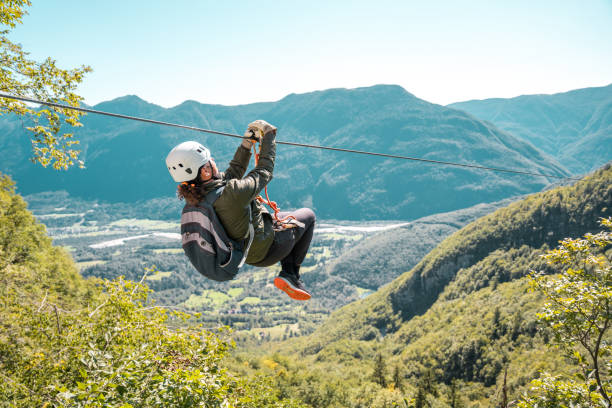 junge frau schwebt auf einer zip-lining-reise in großer höhe in den schönen bergen durch - zip lining stock-fotos und bilder