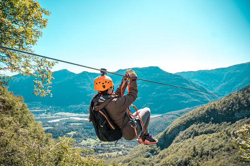Asian female soaring through mountain peaks on an exhilarating zip-line adventure embracing nature's grandeur with breathtaking views and adrenaline-pumping thrills.