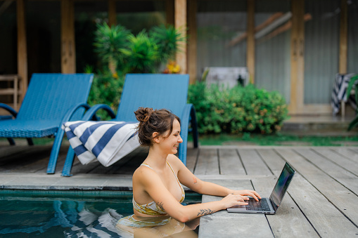 Woman working with laptop from swimming pool on luxuriant villa