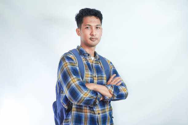 istock Smiling confident young Asian man student wearing casual clothes and backpack folded hands and looking on camera isolated on white background. high school university college concept 2054815456