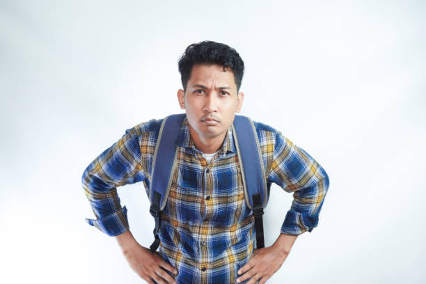 istock angry dissatisfied young Asian student man 20s wearing casual clothes with backpack standing with his hand on his waist on white background. High school university college concept 2054817913