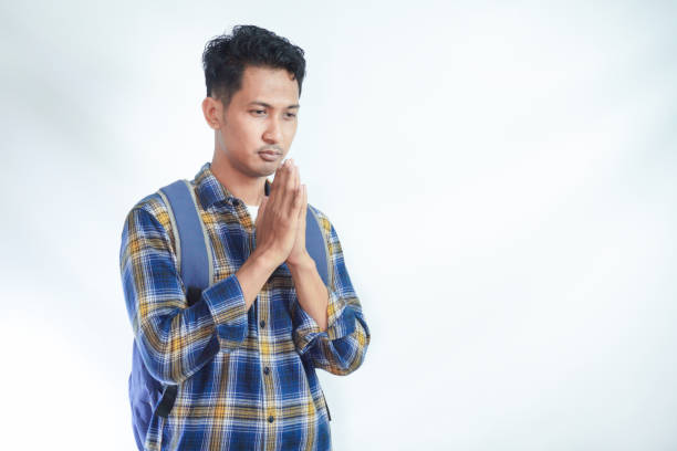istock religious young Asian student man wearing casual clothes with backpack, hand folded in prayer gesture begging about something isolated on white background. High school university college concept 2054822898