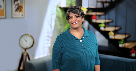 Happy Indian old middle aged smiling businesswoman looking at camera posing for video. Independent beautiful grey-haired  female feminism worker standing at indoor home confidently. Head shot portrait