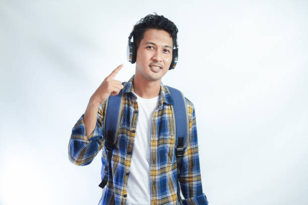 istock Smiling young attractive Asian student wearing casual clothes headphones and backpack standing confident and looking at camera isolated on white background. high school university college concept 2054827621