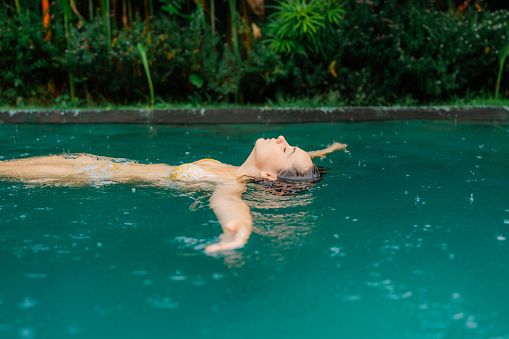 Woman swimming in the pool on villa  during tropical rain on Bali island