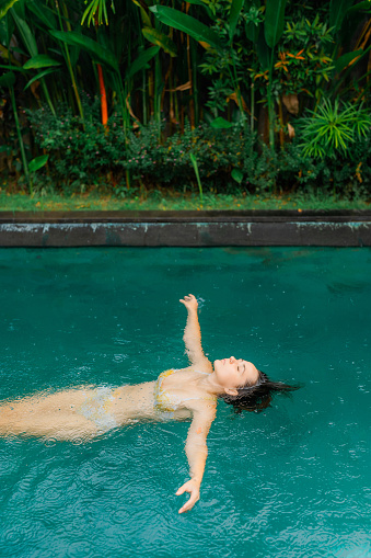 Woman swimming in the pool on villa  during tropical rain on Bali island