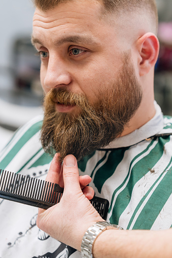 Mid adult man getting his beard trimmed at the local barbershop