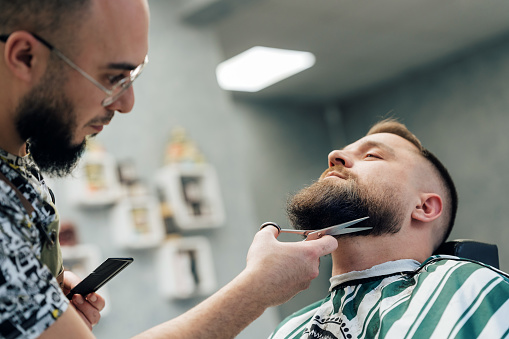 Mid adult man getting his beard trimmed at the local barbershop
