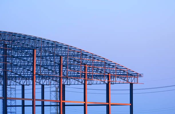 Sunlight reflection on surface of metal industrial warehouse building with dome roof structure in construction site against blue evening sky background at sunset time