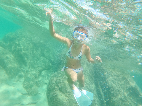Young caucasian girl moving down underwater. She is swimming and diving in clear turquoise colored sea.