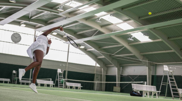 A tennis player holds a racket and ball on a sunlit grass court, preparing for action. Concept of sports intensity and focus in outdoor tennis games.