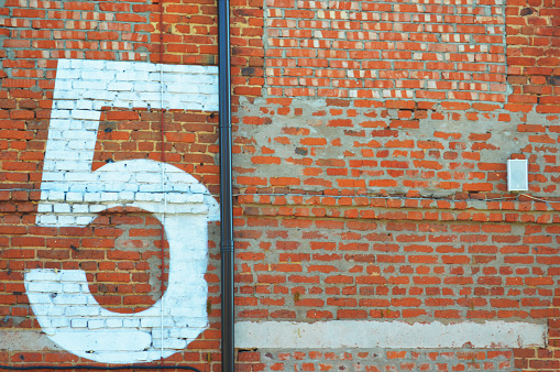 White number five painted on a red brick wall. Number 5.