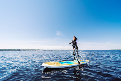 Young adult woman in wetsuit paddleboarding at lake