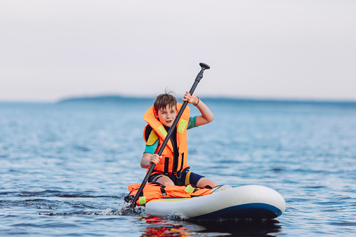 Ten years old boy paddleboarding in wetsuit and life jacket at lake