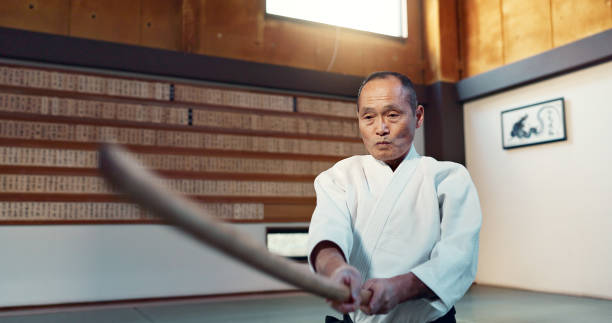 istock Aikido sword, martial arts and mature man strike for training, self defense or combat technique. Dojo, Japanese person and expert with wooden weapon for skills development, attack or bokken practice 2054929609