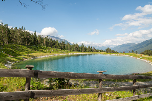 Beautiful summer view of a small alpine lake in the alpine mountains in Imst, Tirol. Water reservoir in beautiful Imst, surrounded by alpine pine trees. Wild flowers and grass. Tranquil scene.