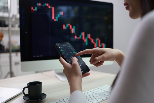 Businesswomen study the financial market to calculate possible risks and profits. Investment applications display stock market charts on the computer screen and advise trading decisions.