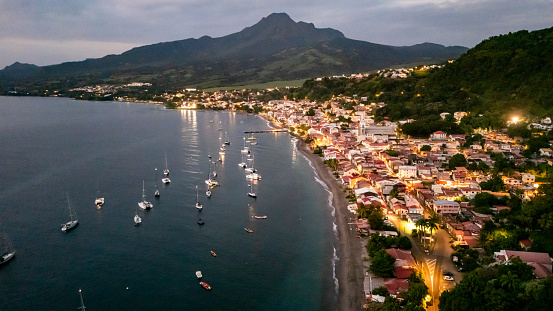 Coastal Town Glimmers with Lights against the Evening Sky,while Boats Gracefully Glide Across the Calm Waters of the Sea,their Illuminated Forms Casting Shimmering Reflections Below,a Scene that Evokes a Sense of Peace and Tranquility as Dusk Settles Over the Picturesque Coastal Landscape.