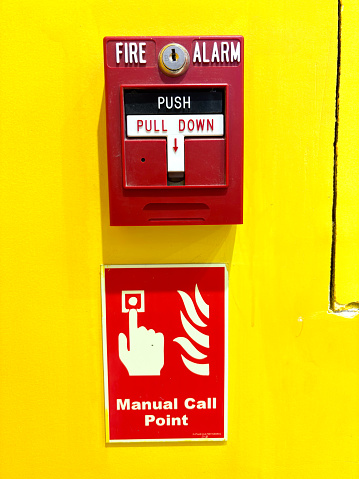 Red fire alarm switch on a vibrant yellow wall with instructions and a manual call point sign.