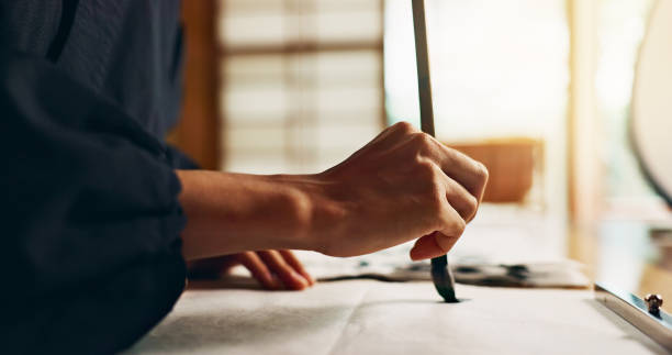 Hands, brush for writing and ancient script for art, calligraphy and closeup with alphabet. Japanese, creativity and vintage tools, paintbrush and stroke with traditional stationery and font