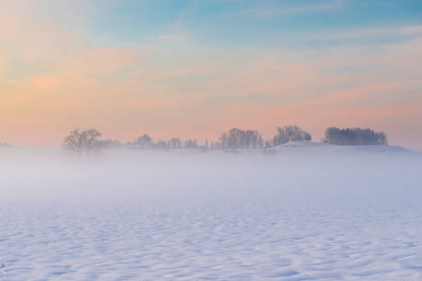 Mist on the ground over a snow-covered hillside landscape on the Mangfall valley in Upper Bavaria at dusk, Germany
