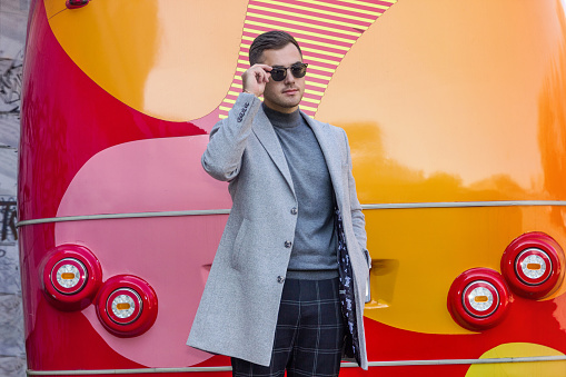 Fashionable man in a gray coat against the background of a red bus. Advertising, luxurious life.
