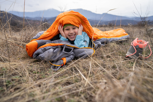 Cute little girl having fun in sleeping bag on a camping trip in nature