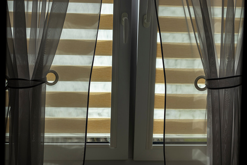 Brightly lit window discreetly covered with a brown roller blind.