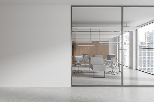 Interior of modern open space office with white walls, concrete floor, rows of computer desks with gray chairs and copy space wall on the left. 3d rendering