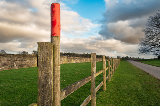 Shallow focus of a red painted post seen along a wooden arable farm fence. An empty road can be seen. Located in mid England near Sherwood Forest.