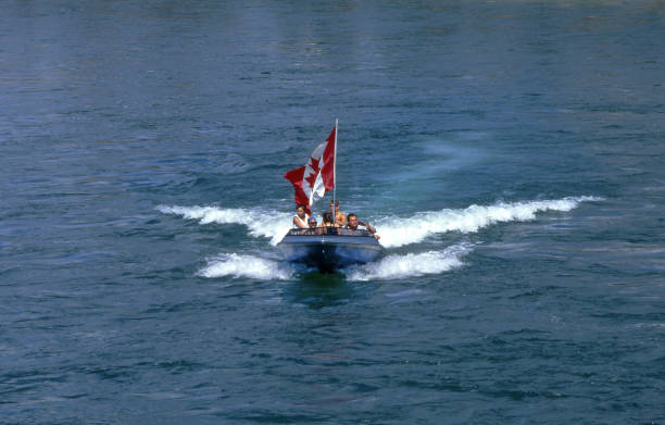 People on board celebrating Canada Day on Whitehorse city in Yukon Territory, Canada - motorboat with canadian flag on surface of Yukon river