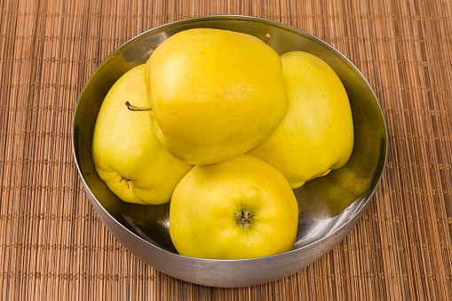 Whole big yellow apples in the stainless steel kitchen bowl on a bamboo table mat