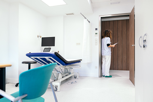 A professional nurse stands by the door, ready to welcome a patient into the medical office.