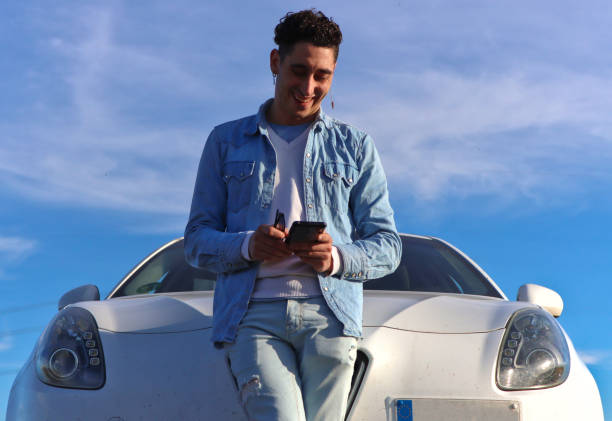 istock Curly haired Caucasian man leaning on his car smiling using mobile 2055129585