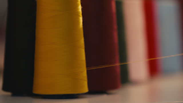 Close-up Of Yellow Sewing Thread Turning Around as It is Being Unwinded In Front Of Other Multicolored Cotton Spools