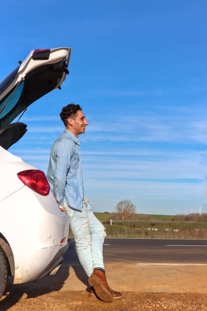 istock Curly Haired Caucasian man leaning on car trunk smiling 2055189559