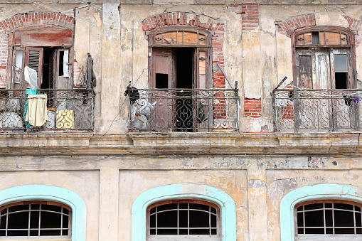 Detail of chipped facade of three-story tenement house in Old Havana with cast iron railing and wooden shutter balconies, closed and open, plastic sacks and buckets, laundry drying. La Habana-Cuba.