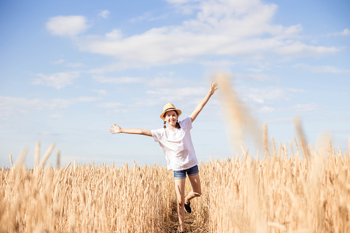 Teenage girl in hat running on field on summer day.