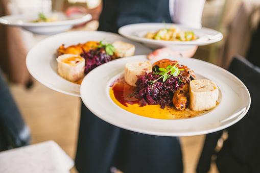 Waiter carrying multiple plates with red cabbage and chicken dish