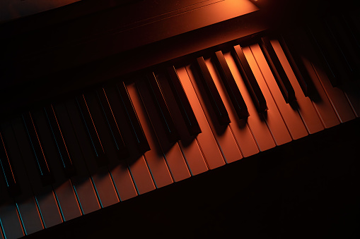Keys of a keyboard instrument (piano, grand piano, synthesizer) with warm orange backlight. Atmospheric live music, evening concert, or relaxing easy listening cover.