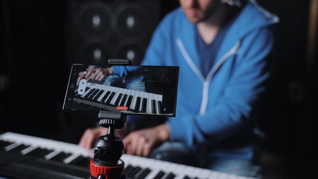 A professional piano player is using his mobile phone to record his performance