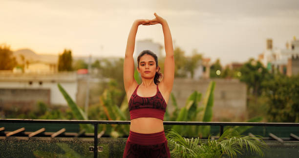 Beautiful Indian gen z woman in sportswear doing workout in bright sunny morning practising different yoga asana at home. Young female stretching exercising warming up body for Fitness at outdoor house hermosa mujer india de la generación z en ropa deportiva haciendo ejercicio en una mañana soleada y brillante practicando diferentes asanas de yoga en casa. mujer joven estirando ejercicio calentando el cuerpo para la aptitud en la casa al aire libre